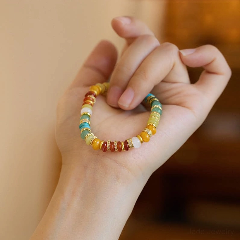 Rainbow jade bracelet held between fingers displaying full bead sequence and copper-plated gold accents
