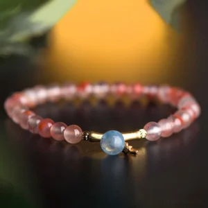 Beaded South Red Agate prosperity bracelet featuring aquamarine drop and gold metal clasp, backlit detail shot
