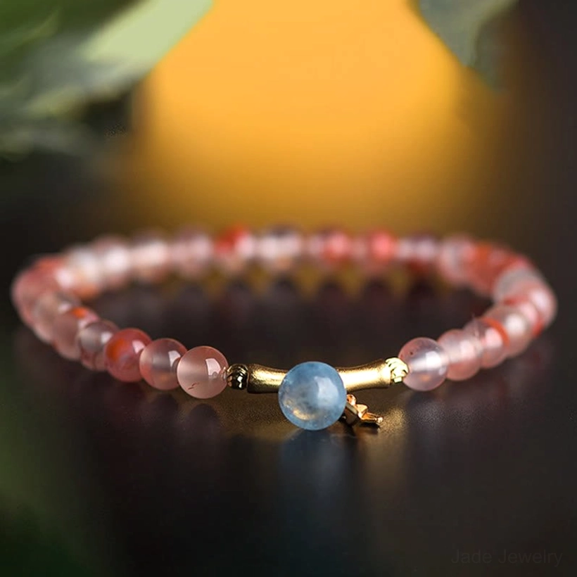 Beaded South Red Agate prosperity bracelet featuring aquamarine drop and gold metal clasp, backlit detail shot