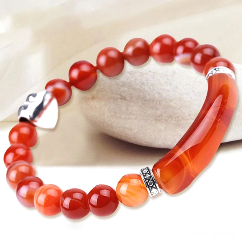 Red agate heart charm bracelet with polished beads and silver heart clasp on light fabric background