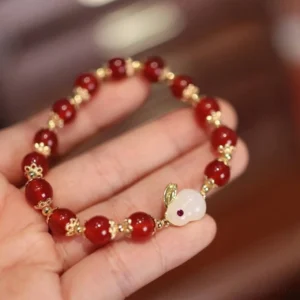 Red agate jade beaded bracelet held in hand showing round beads and gold metal accents against wooden background