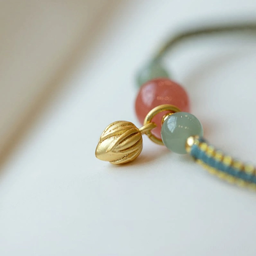 Close-up detail of red agate lotus bracelet charm and gold bud pendant