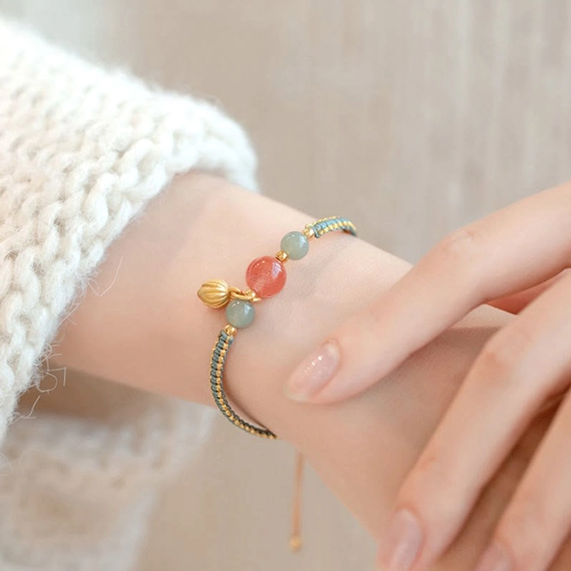 Side angle close-up of red agate lotus bracelet with thin braided rope and gold pendant