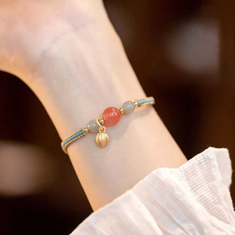 Red agate lotus confidence bracelet worn on wrist with braided string and gold charm pendant