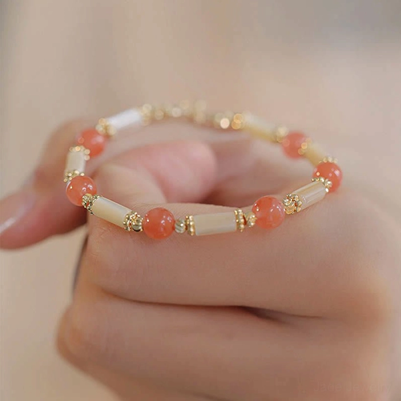 Red agate beaded bracelet with shell beads and gold metal hardware held in hand overhead view, product display