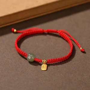 Red string Hetian jade blessing bracelet with adjustable knot and gold fu charm on brown background