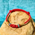 Red string jade couple bracelet with fortune knot, flat lay on stone with gold accents