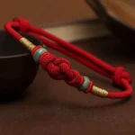 Red string jade fortune knot bracelet handmade with braided red cord, green jade beads, and gold accents - top view display