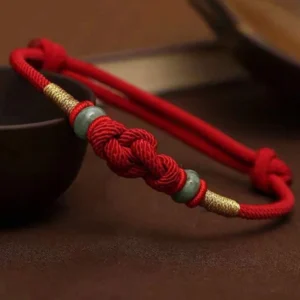 Red string jade fortune knot bracelet handmade with braided red cord, green jade beads, and gold accents - top view display