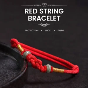 Red string jade fortune knot bracelet with gold accent and natural jade beads, side view on dark display tray