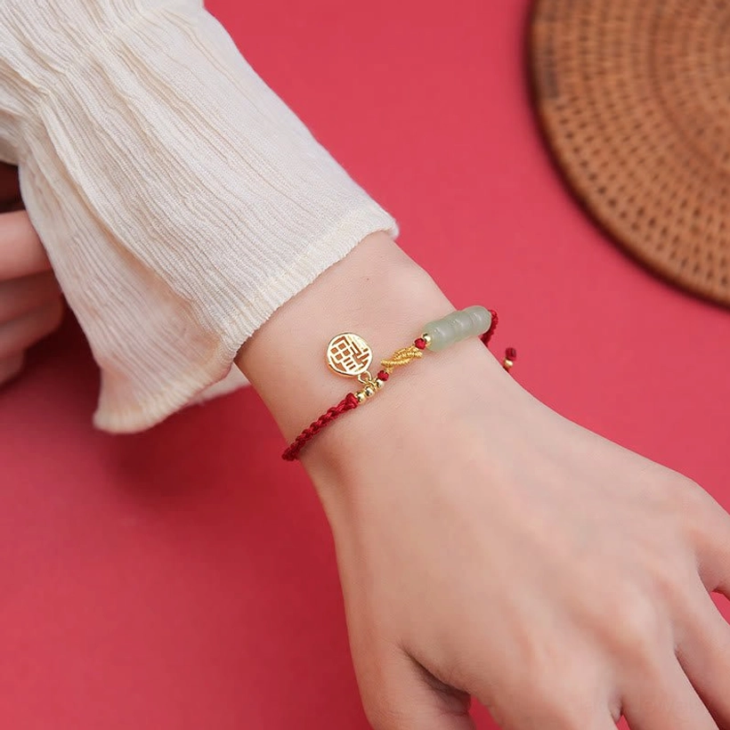 Handcrafted red string jade Fu bracelet worn on wrist with white ruffled cuff - close-up view of polished gold Fu pendant