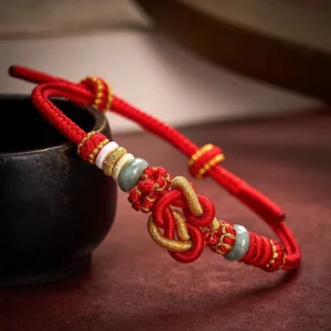 Red jade love heart knot bracelet with gold accents on dark wooden surface
