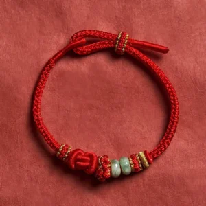 Red jade lucky knot adjustable bracelet with gold accents, flat lay top view