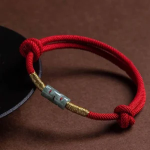 Red jade protection bracelet three-quarter angle view on display stand, showing woven rope construction and jade bead detail