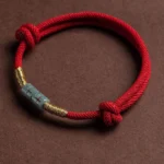 Red jade string rope bracelet with gold accents, flat lay view featuring adjustable decorative knots and polished jade centerpiece