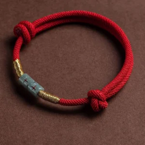 Red jade string rope bracelet with gold accents, flat lay view featuring adjustable decorative knots and polished jade centerpiece