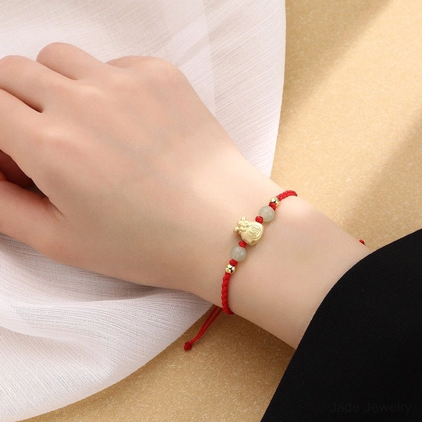 Red rope jade prosperity bracelet worn on wrist showing adjustable pull cord, gold Fu character charm, and jade bead details in first-person wear view