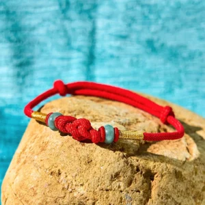 Red braided string jade bracelet with central knot detail and gold wraps on stone