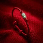 Close-up of handmade red string jade protection bracelet with polished green jade beads and adjustable sliding knot on red knitted fabric