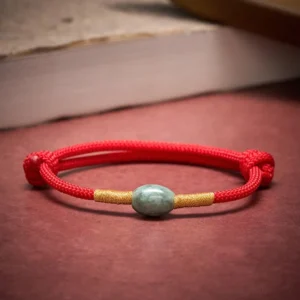 Red string jade bracelet front view on red table with book background highlighting braided cord and jade stone detail
