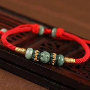 Handmade jade beads on red rope bracelet, overhead view showing decorative woven knots and gold thread details