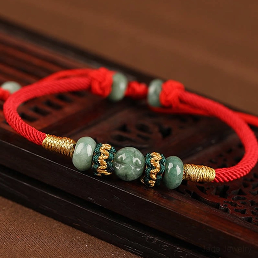 Handmade jade beads on red rope bracelet, overhead view showing decorative woven knots and gold thread details