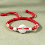 Red string jade prosperity bracelet with white jade bead and decorative knots, flat lay top-down view on light background