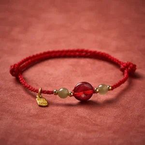 Adjustable red braided cord bracelet with cinnabar bead, jade beads and gold Fu pendant charm overhead view
