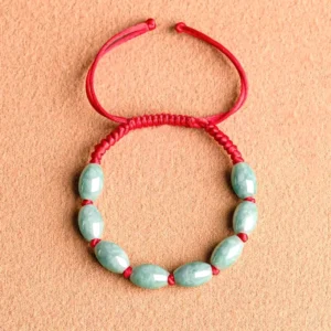 Overhead view of red string jade bracelet with oval green jade beads and adjustable sliding knot on terracotta background