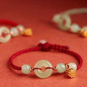 Adjustable red cord jade bracelet with braided knot, gold lotus pendant, and jade charm set - shallow focus overhead shot