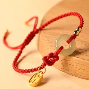 Red string jade bracelet with peace buckle and fu character charm displayed on wooden base, side angle showing adjustable slip-knot design