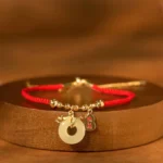 Red string jade peace buckle bracelet with fu character charm on wooden display, showing gold-plated hardware and light jade pendant