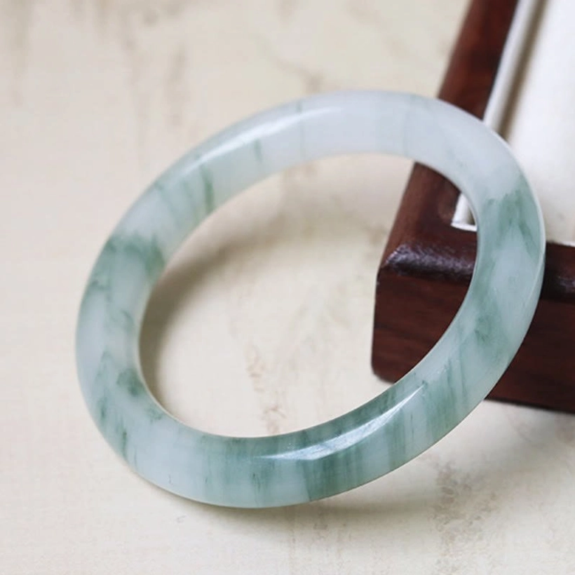 Single natural jade bangle bracelet close-up side view with green marbled pattern on pale jade and polished smooth surface