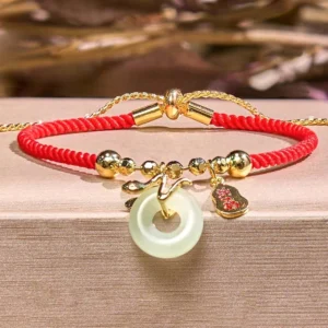 Year of the Snake red string luck bracelet with adjustable sliding clasp, dual red ropes, jade peace buckle and fu charm on wooden platform