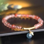 South Red Agate bamboo charm bracelet with aquamarine leaf pendant on black minimalist background, overhead view