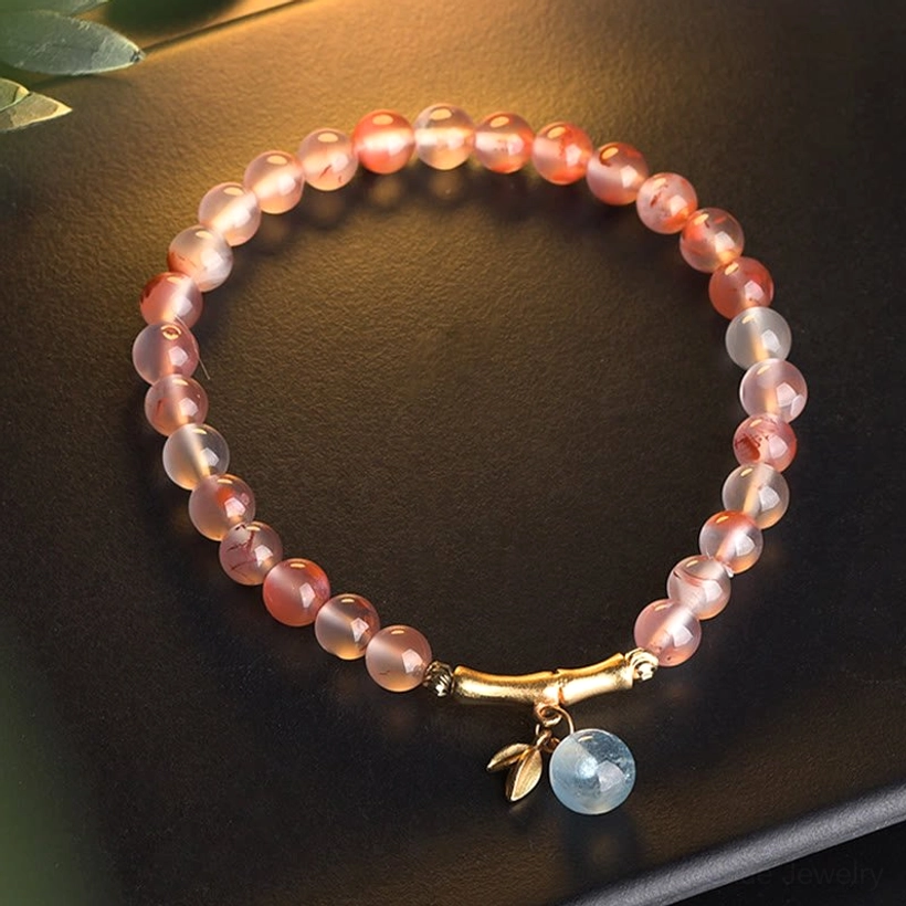 South Red Agate fortune bracelet with gold bamboo clasp and blue aquamarine pendant, flat lay on glossy surface