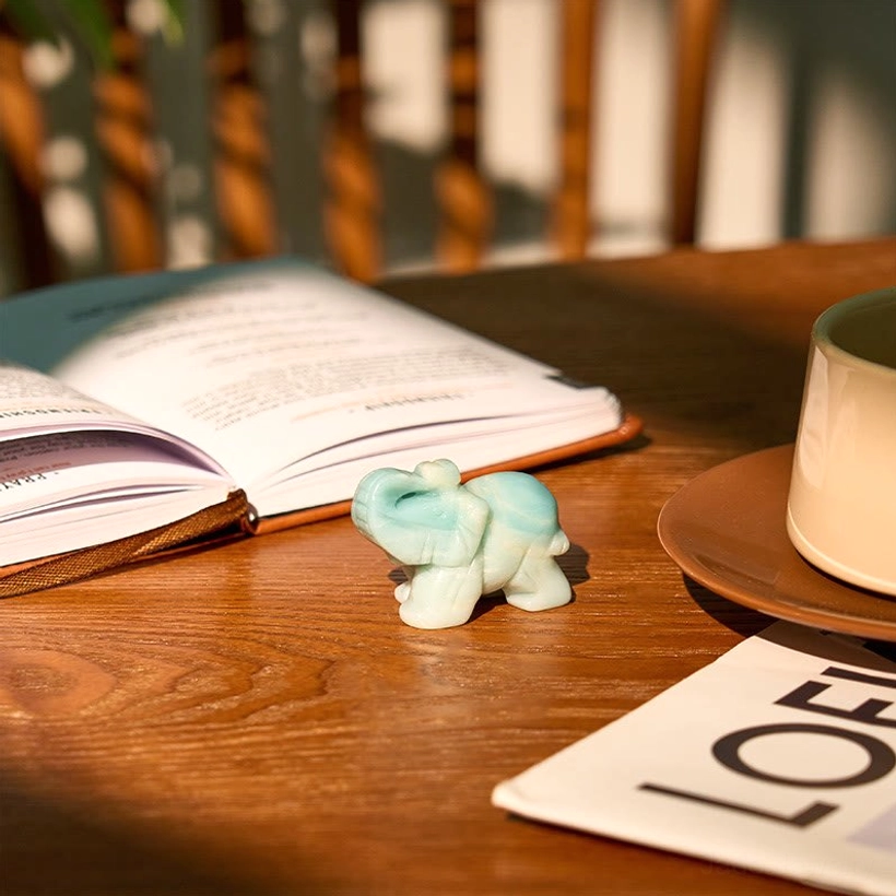 Carved amazonite elephant positioned next to book and coffee cup on wooden study desk
