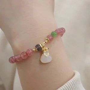 Strawberry quartz healing bracelet worn on wrist with white jade money bag pendant charm, close-up side view
