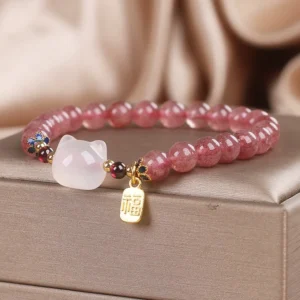 Flat lay view of healing crystal bracelet featuring pink strawberry quartz beads, white jade cat charm, and gold Fu character pendant