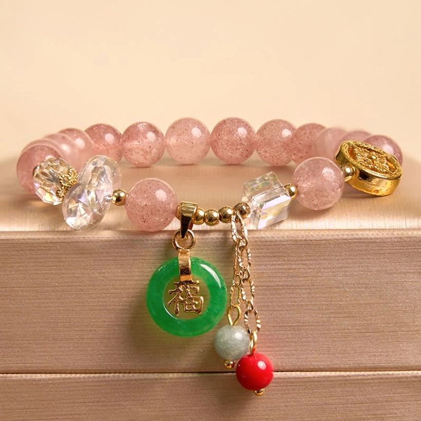 Close-up overhead view of strawberry quartz Fu character bracelet with pink beads green jade charm and crystal accents