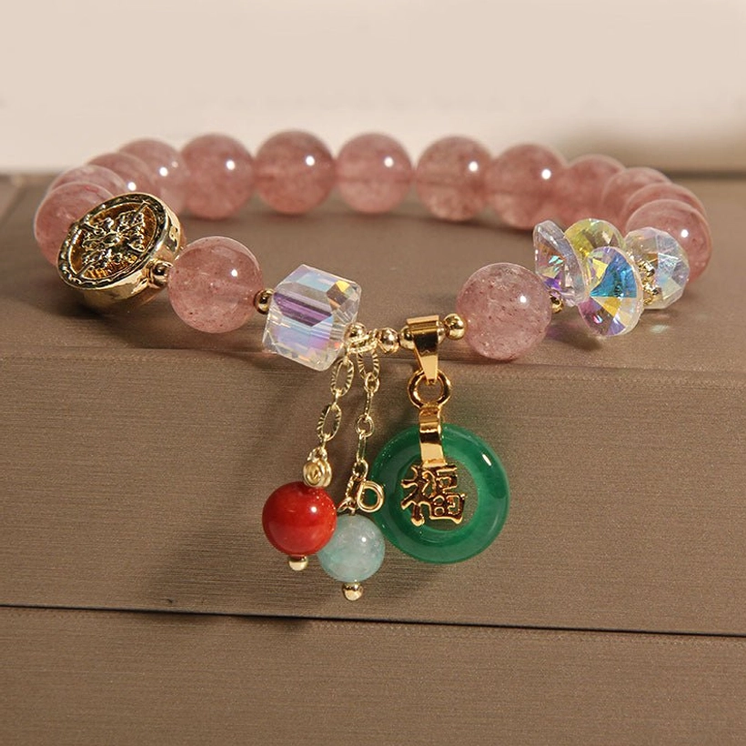 Strawberry quartz Fu charm bracelet overhead on brown cardboard with pink beads green jade and gold metal accents