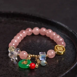Flat lay view of strawberry quartz healing bracelet with gold hardware and crystal accents on black tray