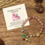 Strawberry quartz jade Fu charm bracelet flat lay with gift card and decorative pinecones on wooden surface