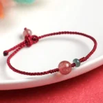 Strawberry quartz jade red string bracelet with adjustable knot closure on white plate with red background
