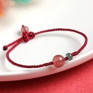 Strawberry quartz jade red string bracelet with adjustable knot closure on white plate with red background