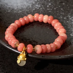 Strawberry Quartz Cyan Jade lucky cat bracelet on black ceramic plate showing round pink beads and gold charm