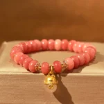 Strawberry Quartz lucky cat beads bracelet top-down flat lay with pink rondelle beads and gold lucky cat charm on wooden display