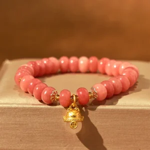 Strawberry Quartz lucky cat beads bracelet top-down flat lay with pink rondelle beads and gold lucky cat charm on wooden display