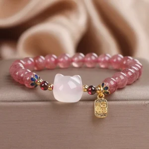 Strawberry quartz white jade cat Fu bracelet with gold pendant shown from overhead angle on luxury display box