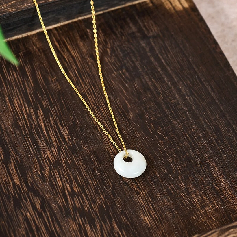 Delicate thin gold chain jade necklace displayed on dark wooden table, top-down view